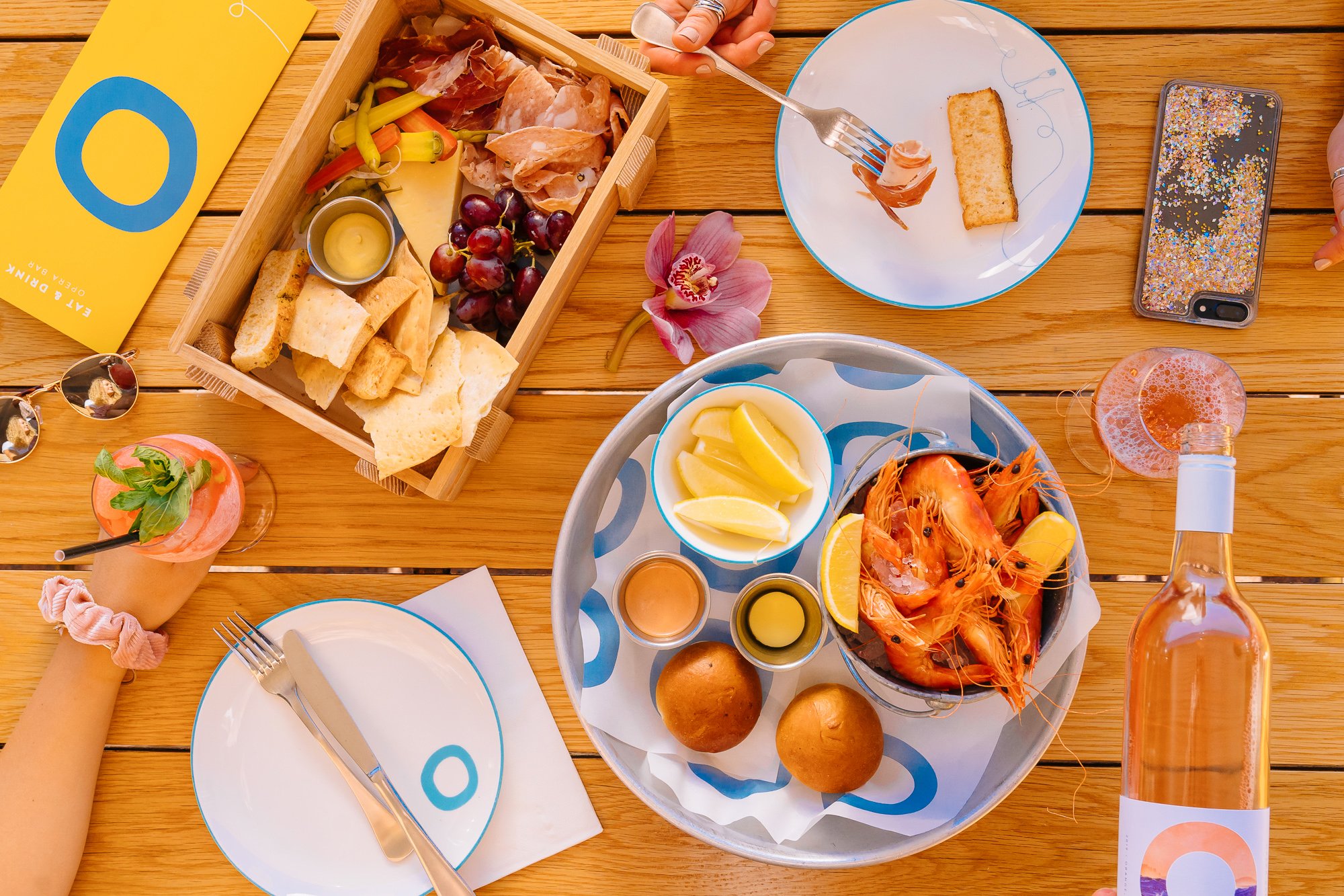 Flat lay of a cheeseboard, wine, cutlery, plates and prawns