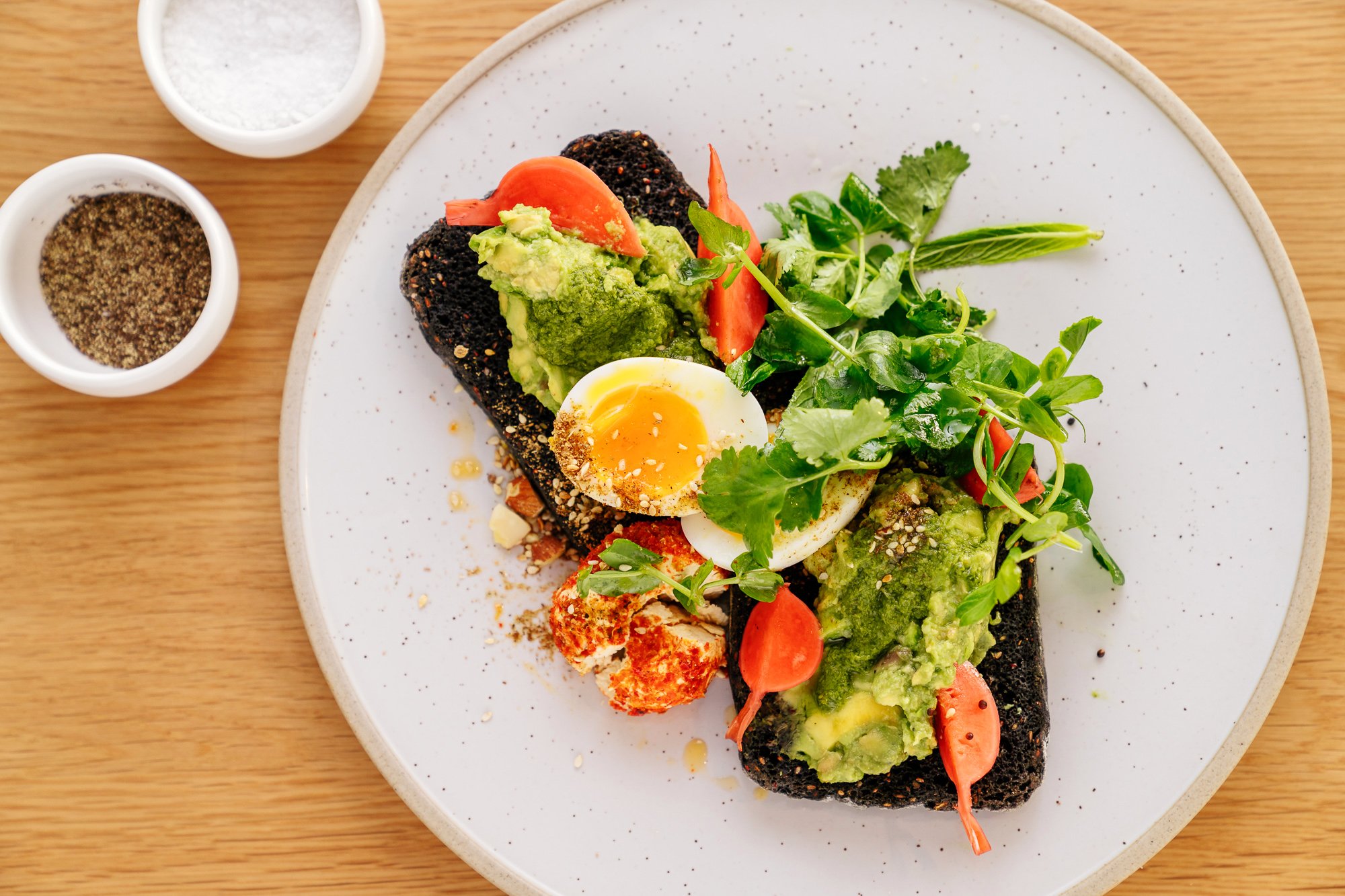 Avocado and soft boiled eggs on toast, surrouded with garnishes