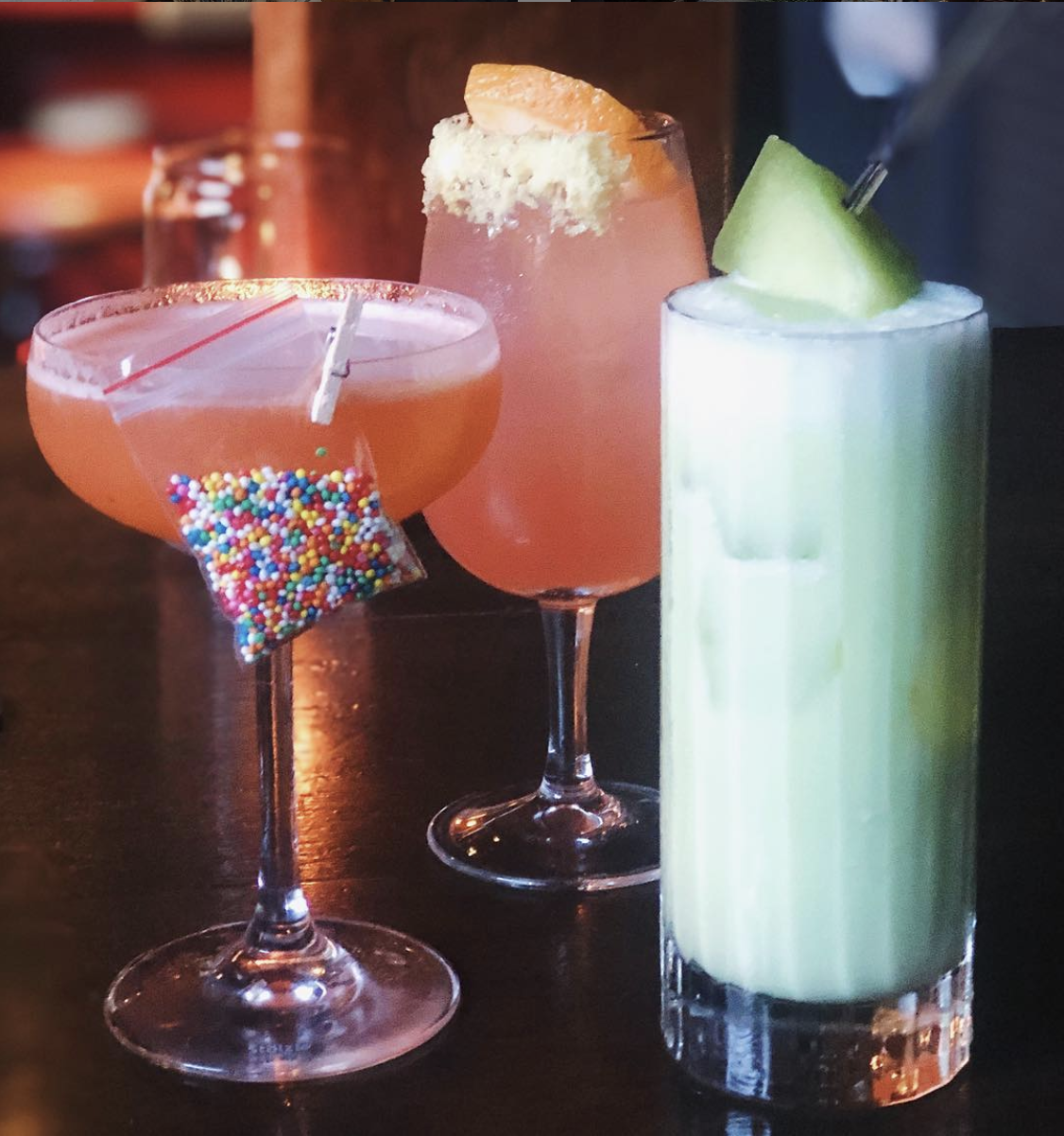 Three colourful cocktails in all different glass shapes, garnished with fruits and sprinkles