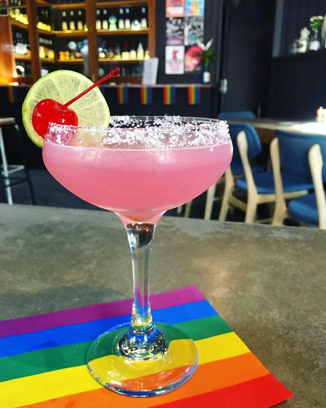 A bright pink margarita cocktail on a rainbow coaster